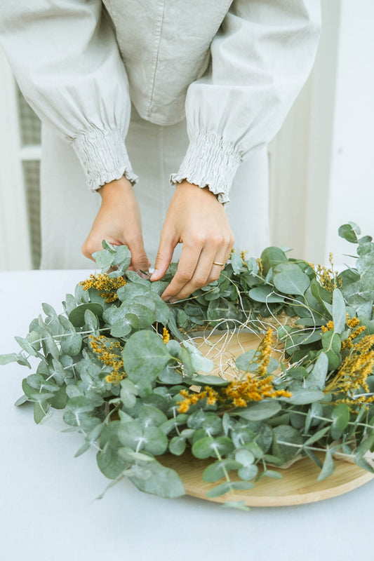 Person arranging greenery on a wooden plate with a blurred background