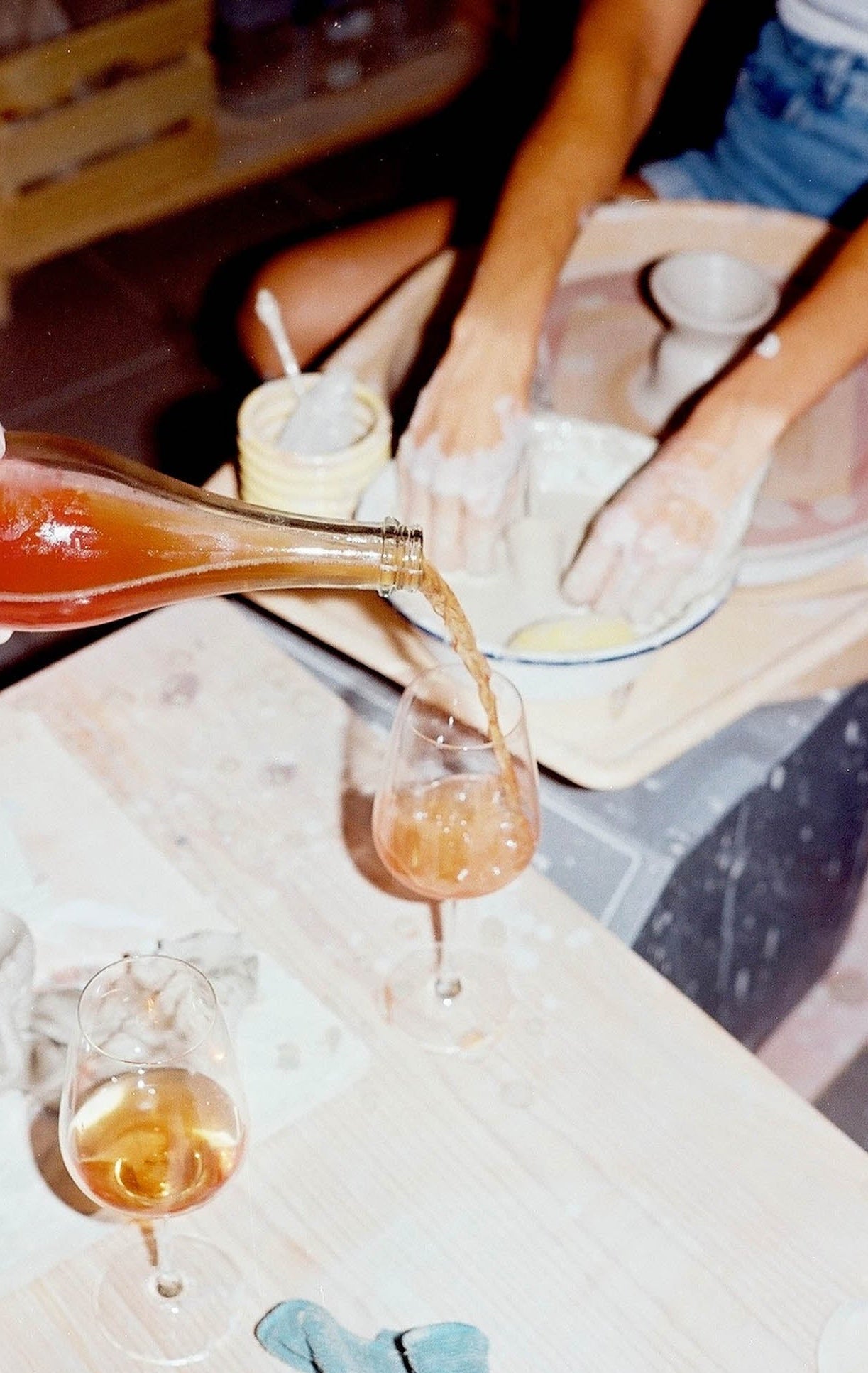 Person pouring a drink into a glass on a wooden table.