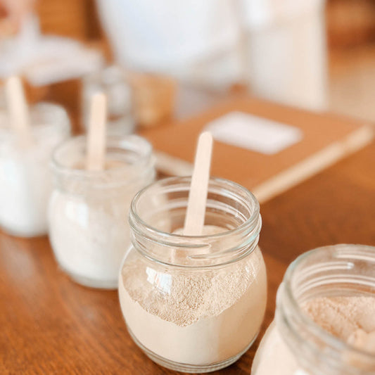 Glass jars with powders and wooden sticks on a wooden surface