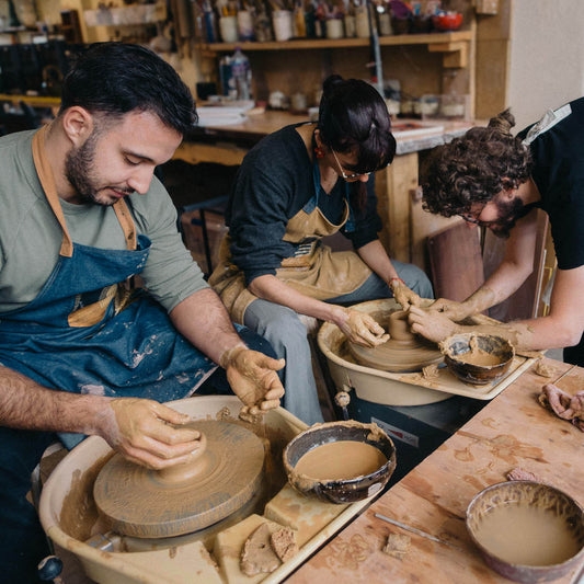 Three people working with clay in a pottery studio.