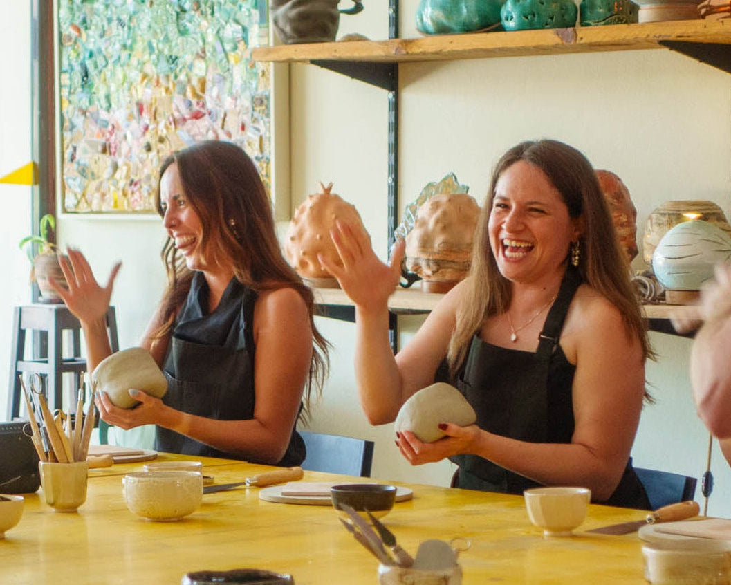 Group of people in a pottery studio with clay pots and tools on a table.