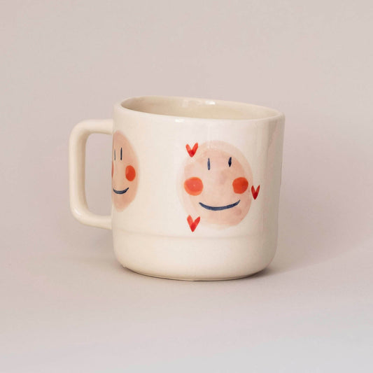 White mug with cartoon faces on a light gray background