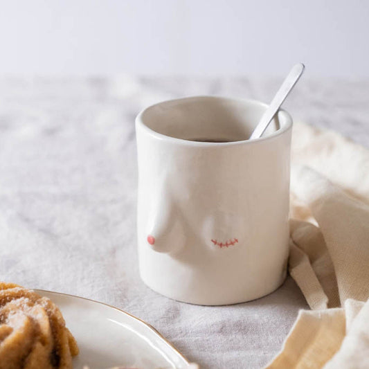 A white ceramic cup with a floral design, placed on a table with a cake and a spoon, suggesting a warm and inviting atmosphere.