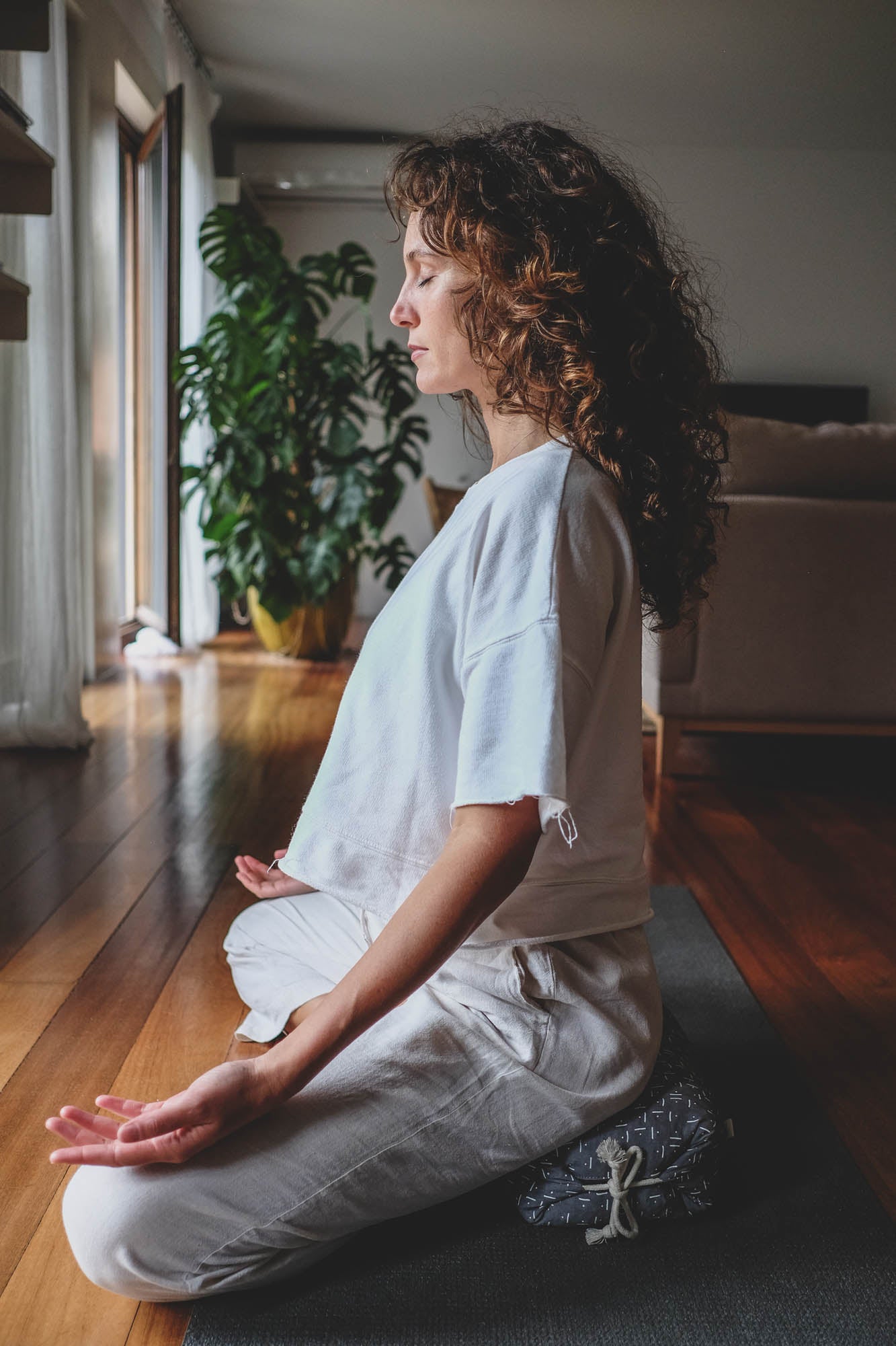 Woman meditating on a cushion in a room with plants.