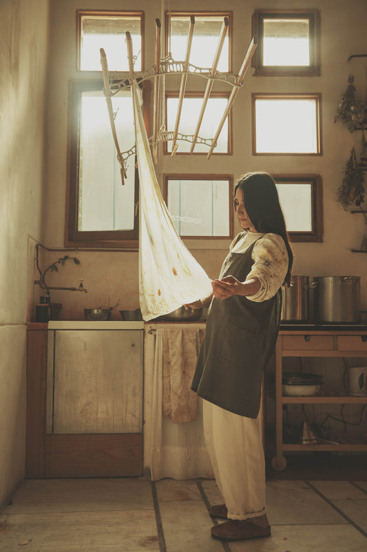 Person standing in a kitchen holding a white cloth, with large windows letting in natural light.