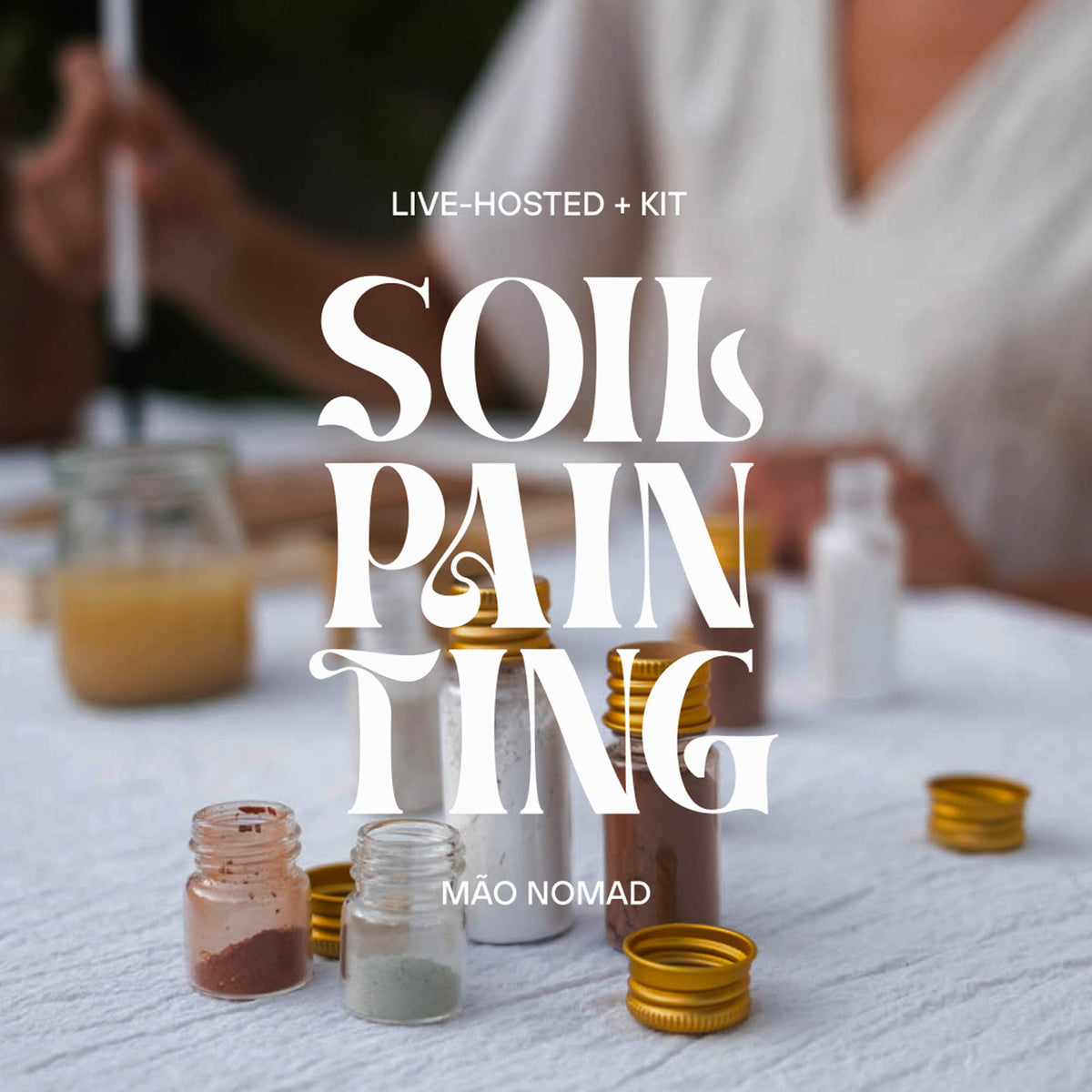 Promotional graphic for a 'Soil Painting' kit by Mão Nomad, featuring large white stylized text over a blurred lifestyle scene of a person painting at a table with small jars of paint and gold bottle caps.