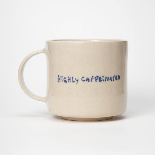 Beige mug with 'HIGHLY CAFFEINATED' text in blue on a white background