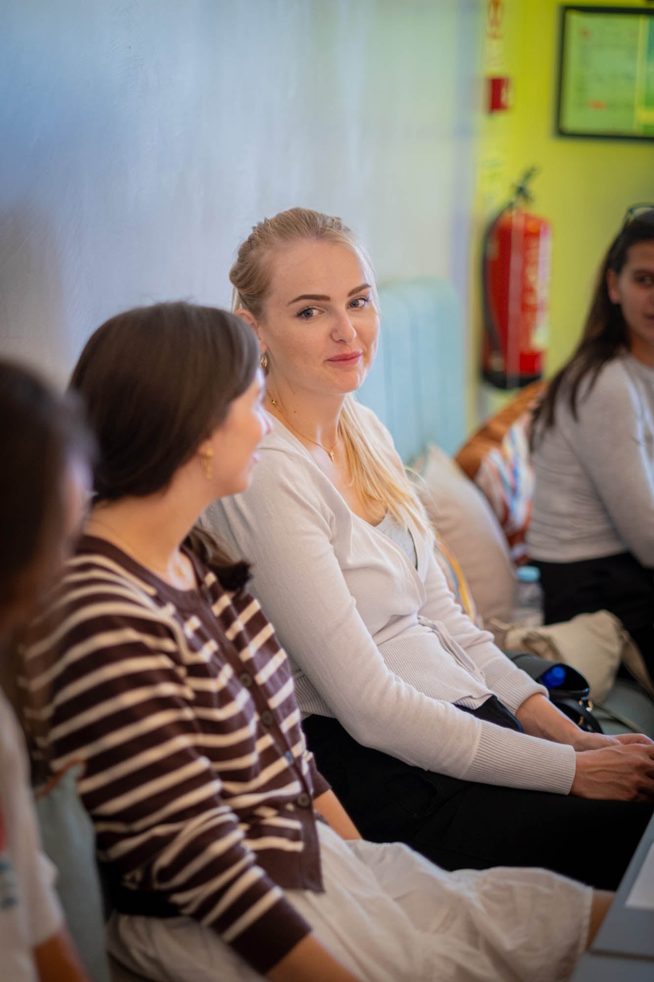 Woman sitting in a classroom or meeting room with other people.