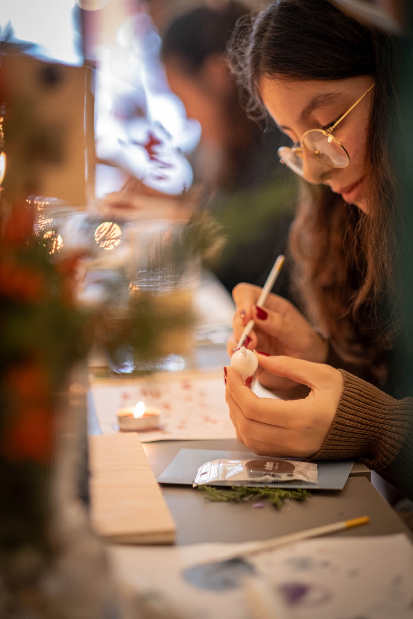 Woman painting a small object with a brush at a table.