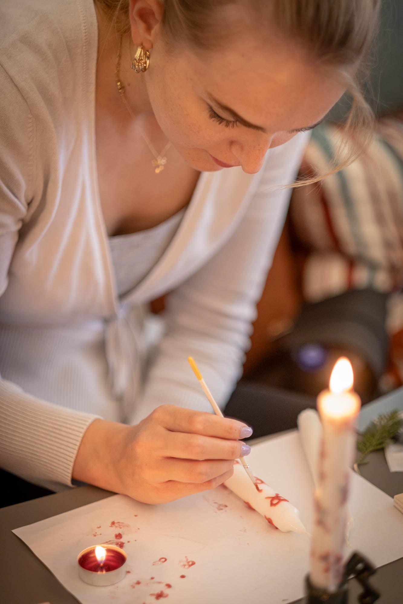 Woman lighting a candle with a match on a table.