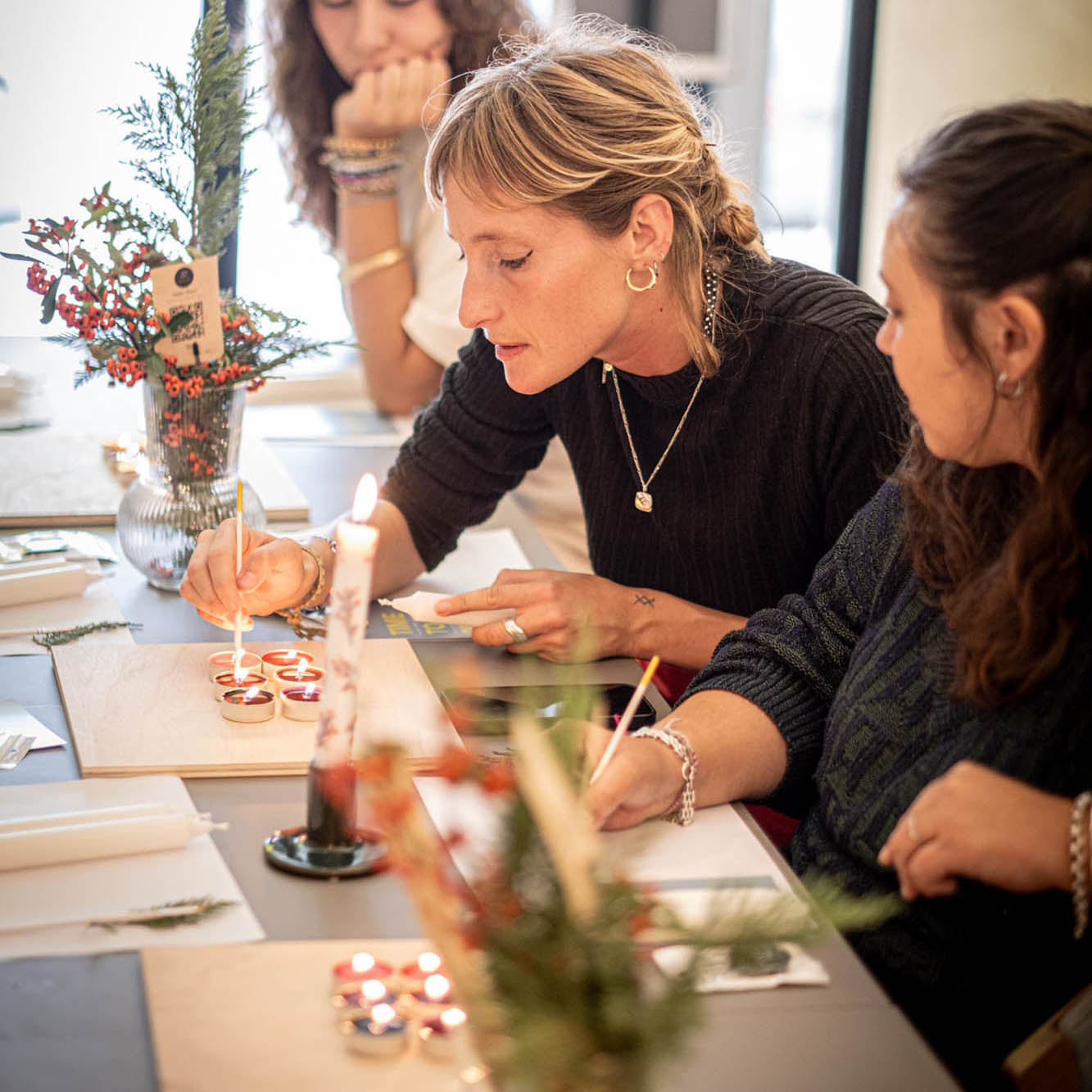 Two women sitting at a table with candles and paper, possibly in a workshop or class setting.