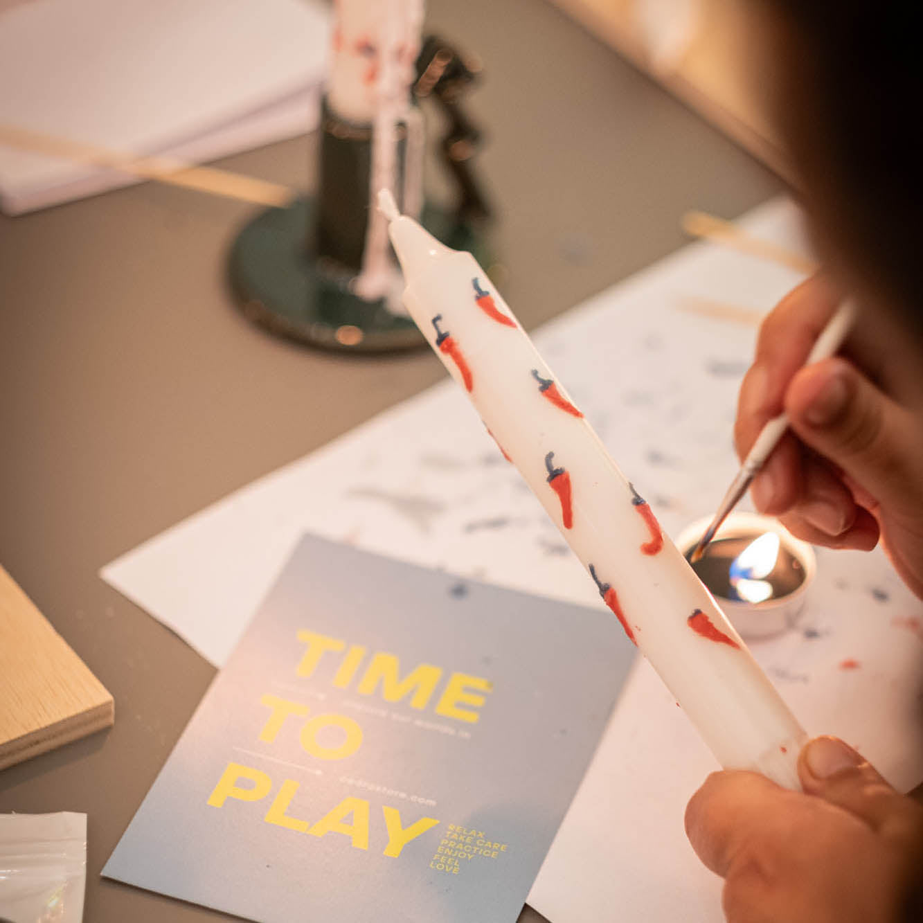 Person lighting a candle with a 'Time to Play' postcard on a table