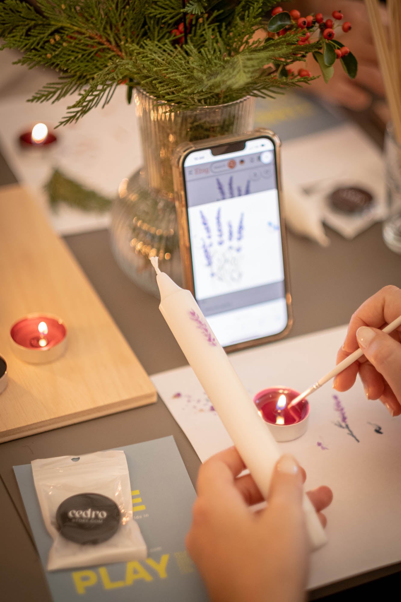 Person using a smartphone app to light a candle with a lit candle and phone in the background.
