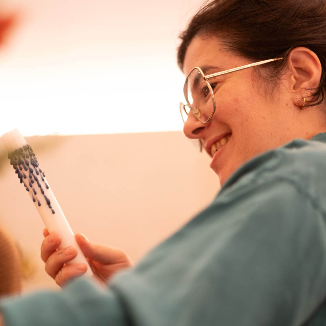 Person holding a white object with a pattern, wearing glasses and a green shirt.
