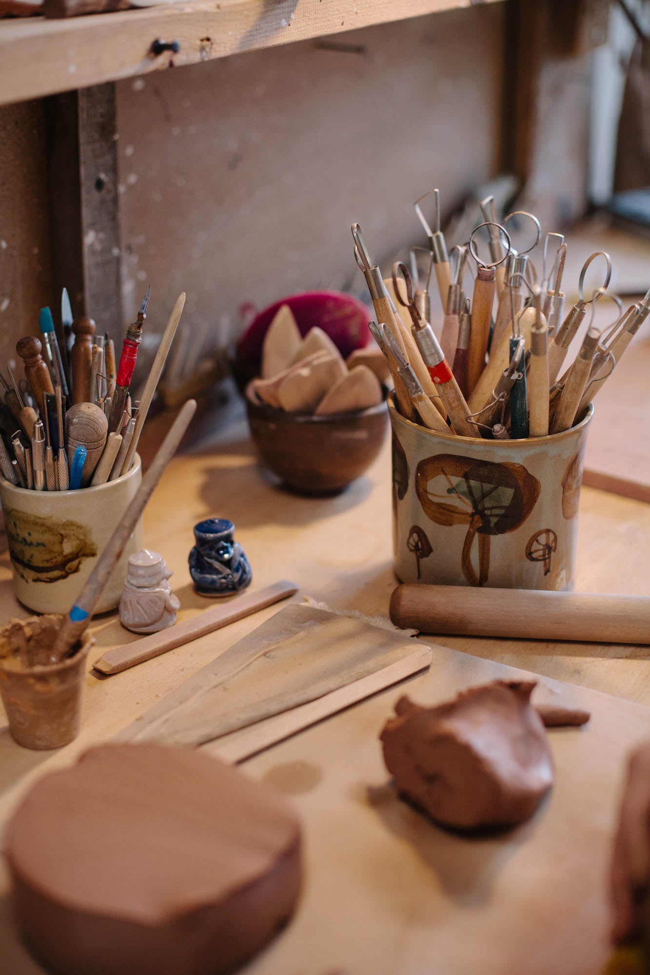 Clay modeling tools and clay on a wooden table in a workshop setting.