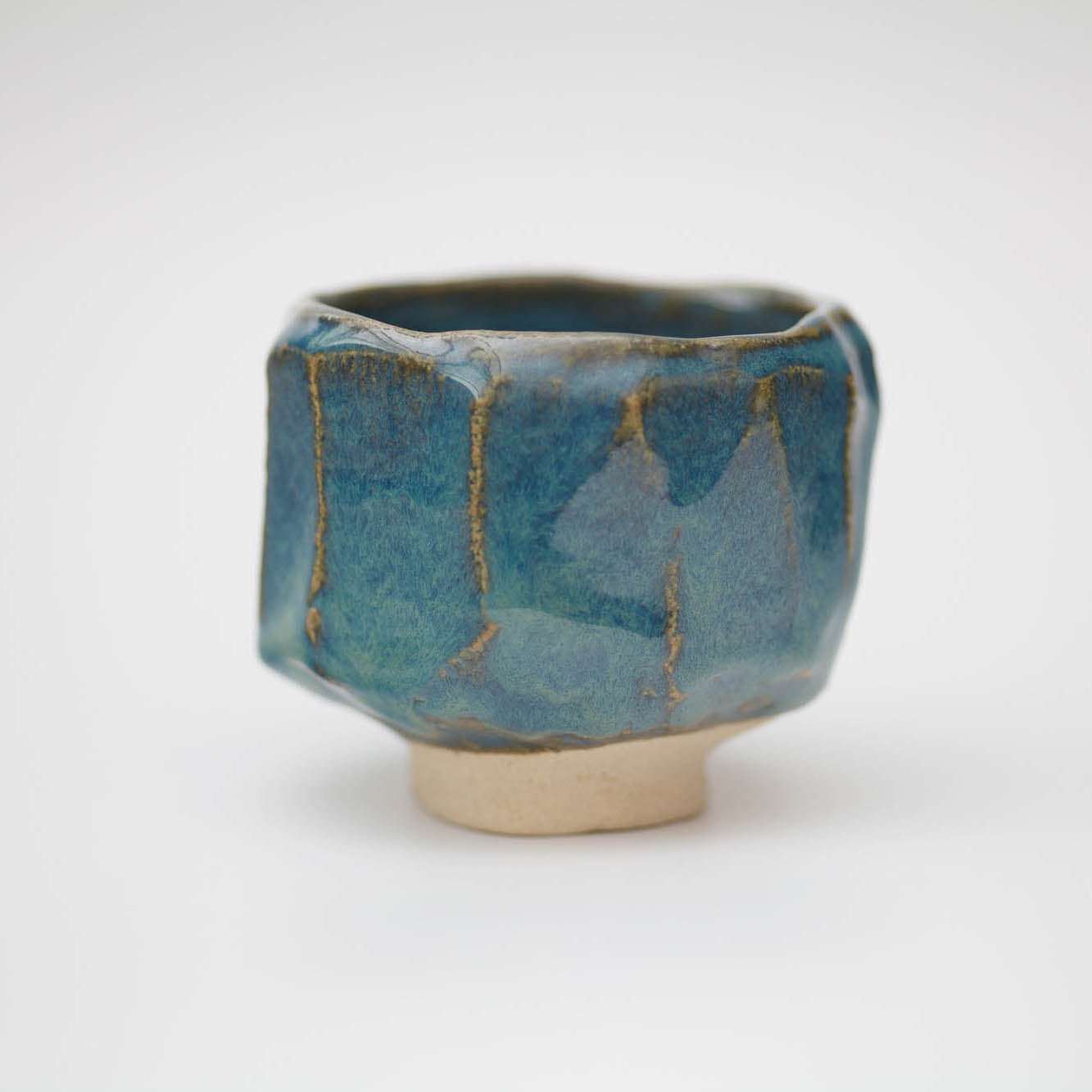 Hexagonal ceramic cup with blue glaze and beige base on a white background