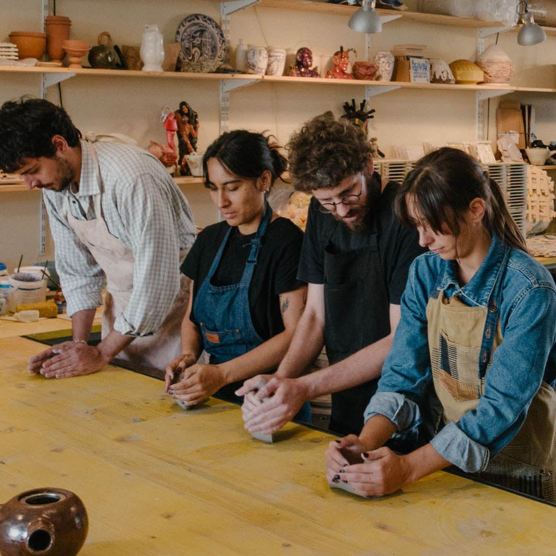 Group of people working together in a pottery studio with shelves and tools in the background.