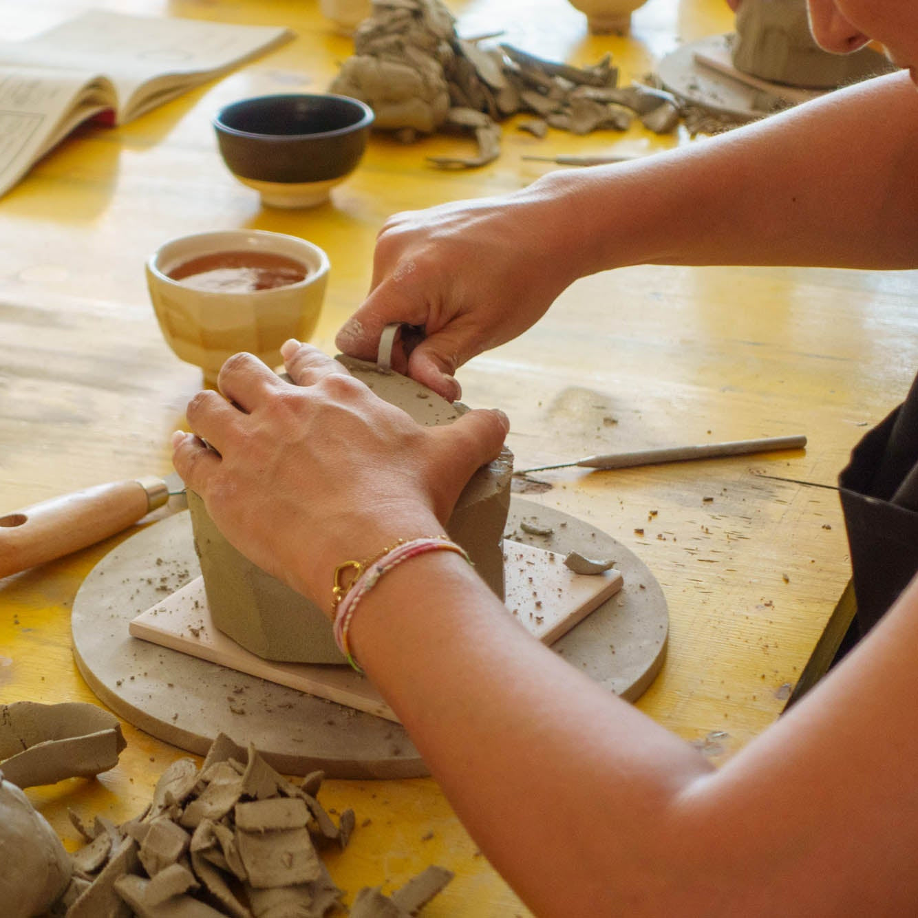 Person working with clay on a pottery wheel in a workshop setting.