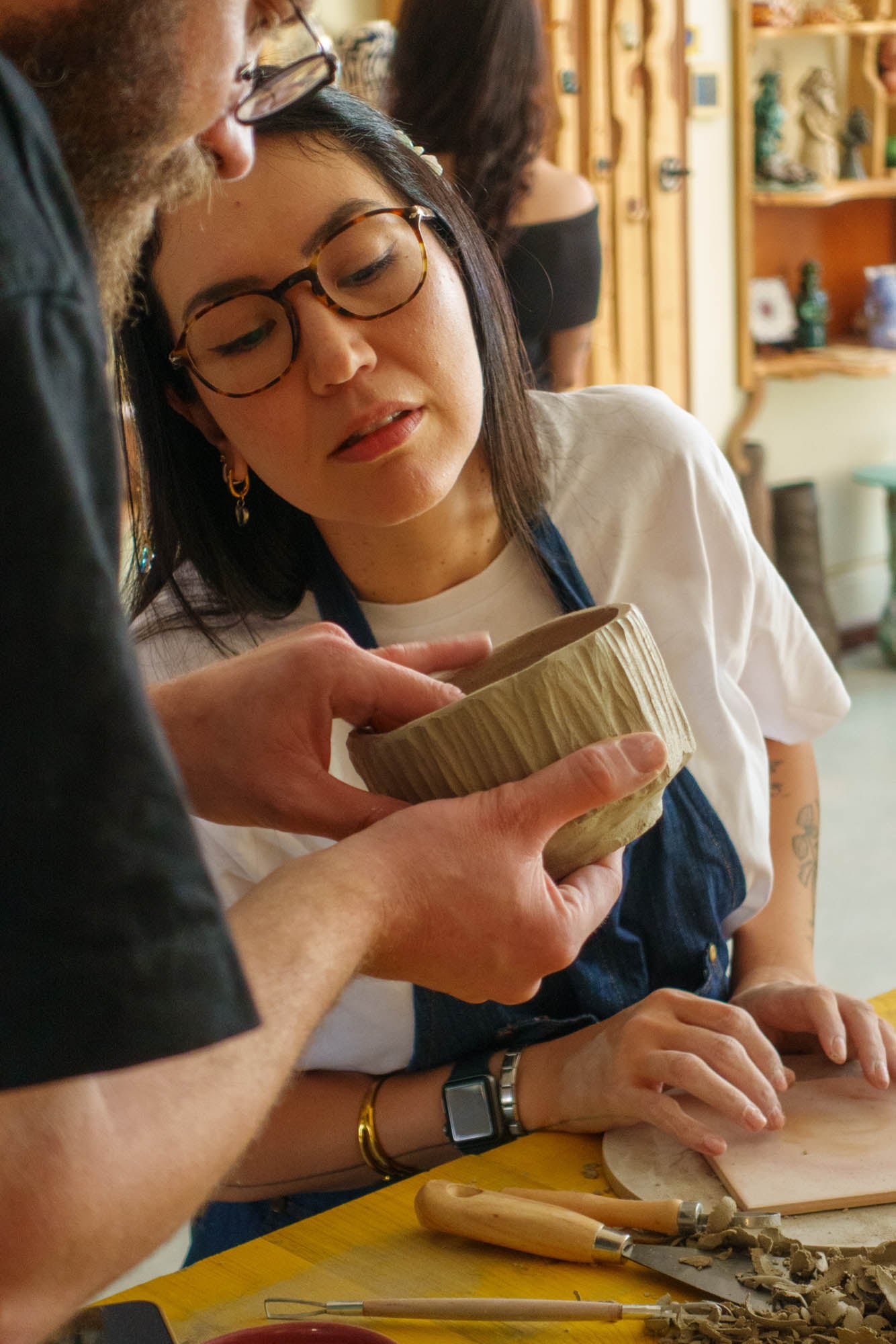 Two people examining a small ceramic bowl at a table with tools and materials.