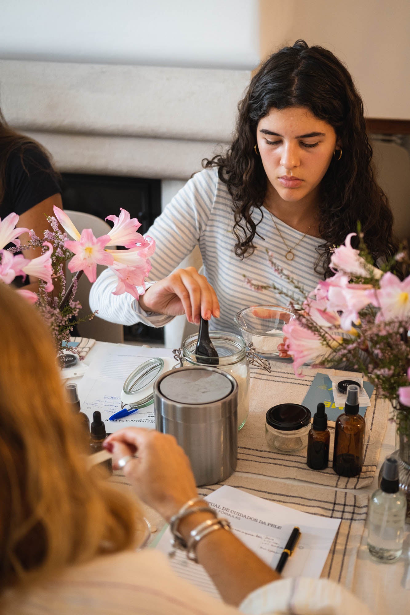 Two women at a table with candles and floral arrangements, possibly in a workshop setting.