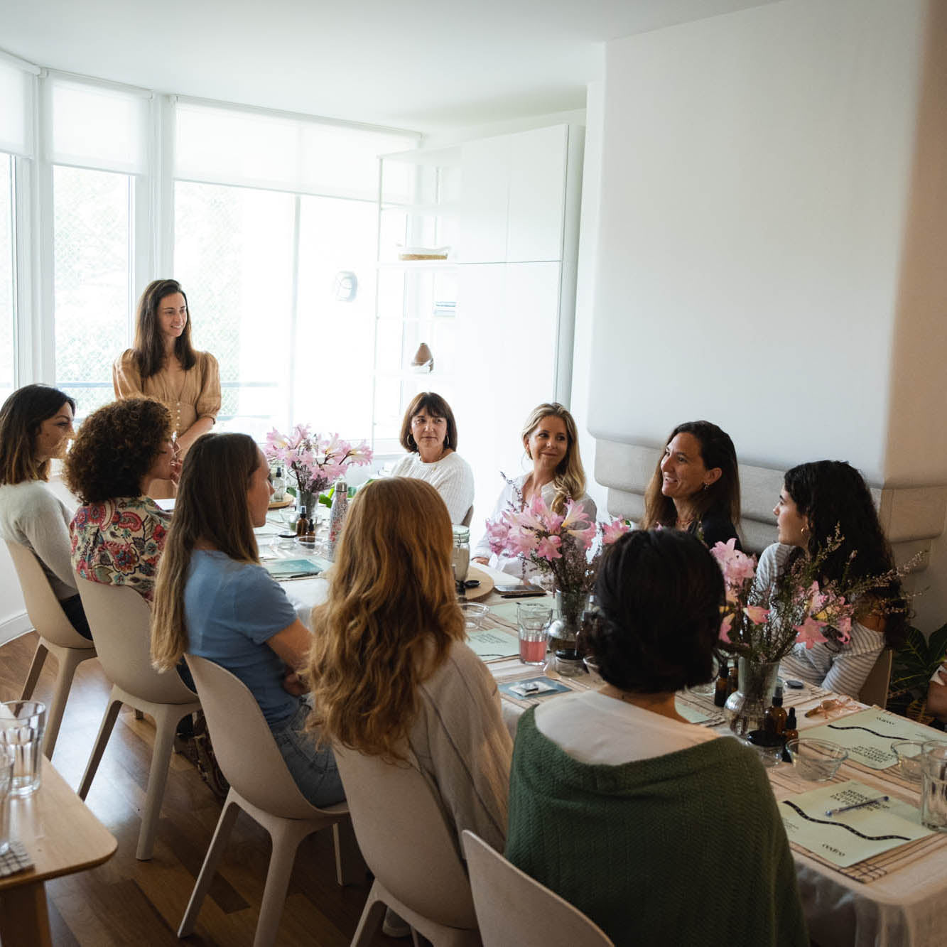 Group of women sitting around a table with floral arrangements in a bright room.