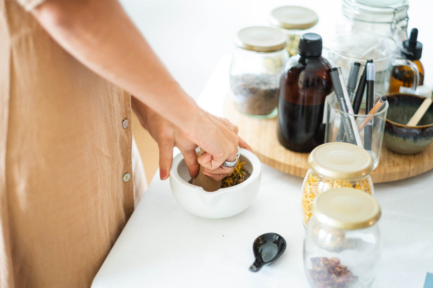 Person preparing a herbal concoction with various jars and bottles on a table.