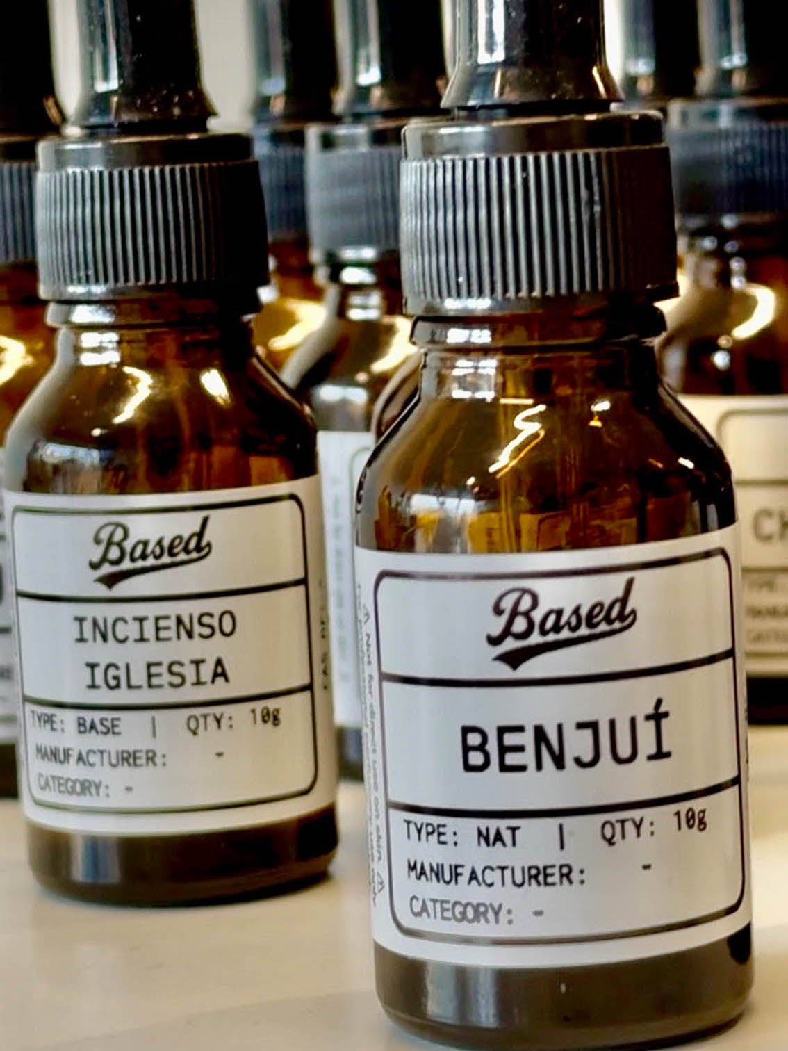 Two amber glass dropper bottles with black caps and white labels from the brand Based, featuring 'INCENSO IGLESIA' and 'BENJUI' scents, shown in a close-up arrangement.