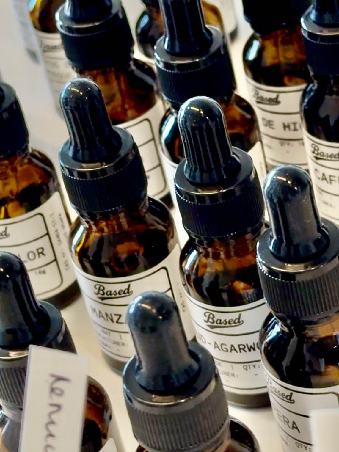 Multiple amber glass dropper bottles with black droppers and white labels arranged closely together on a light surface. 