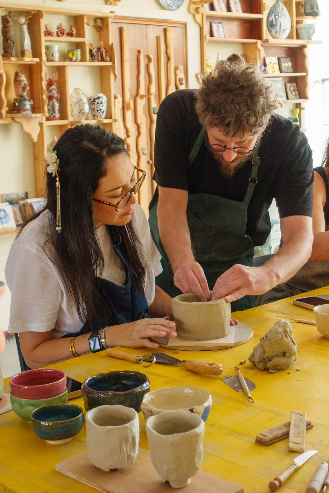 Two people working on pottery at a table with various ceramic items.