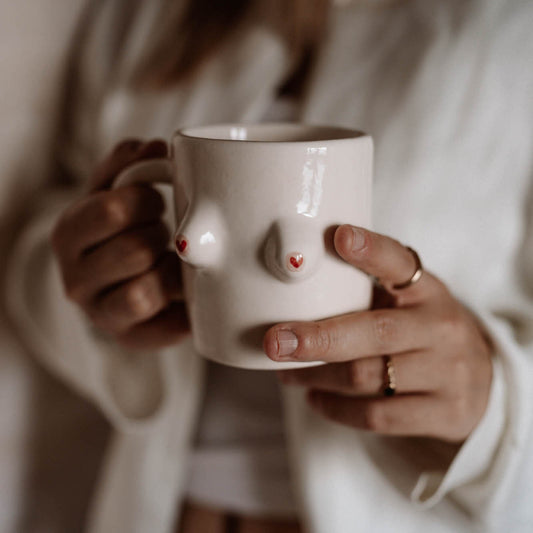Person holding a white mug with a cartoonish face design.