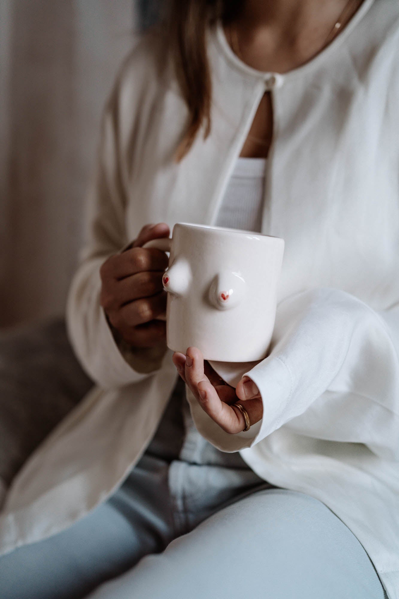 Person holding a white mug with a cat design, wearing a white sweater and light blue pants.