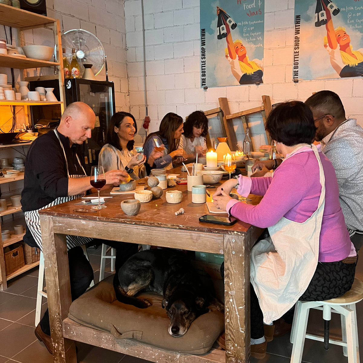Group of people sitting around a wooden table in a cozy kitchen setting, with a dog on a cushion.