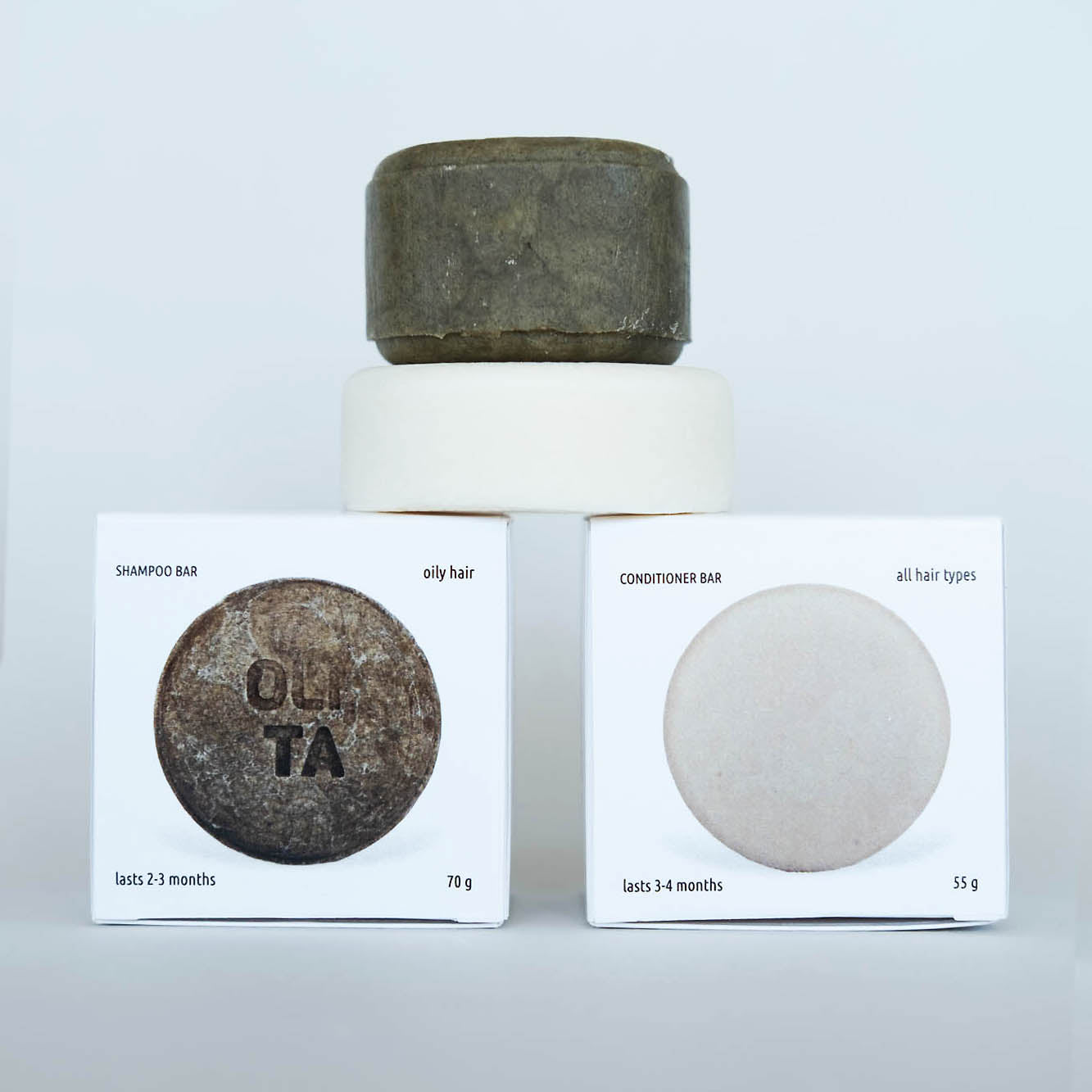 Ollta KIT hair care bars stacked on top of their white retail boxes against a light gray background. The stack includes a oily hair shampoo bar on top and a conditioner bar in the middle-